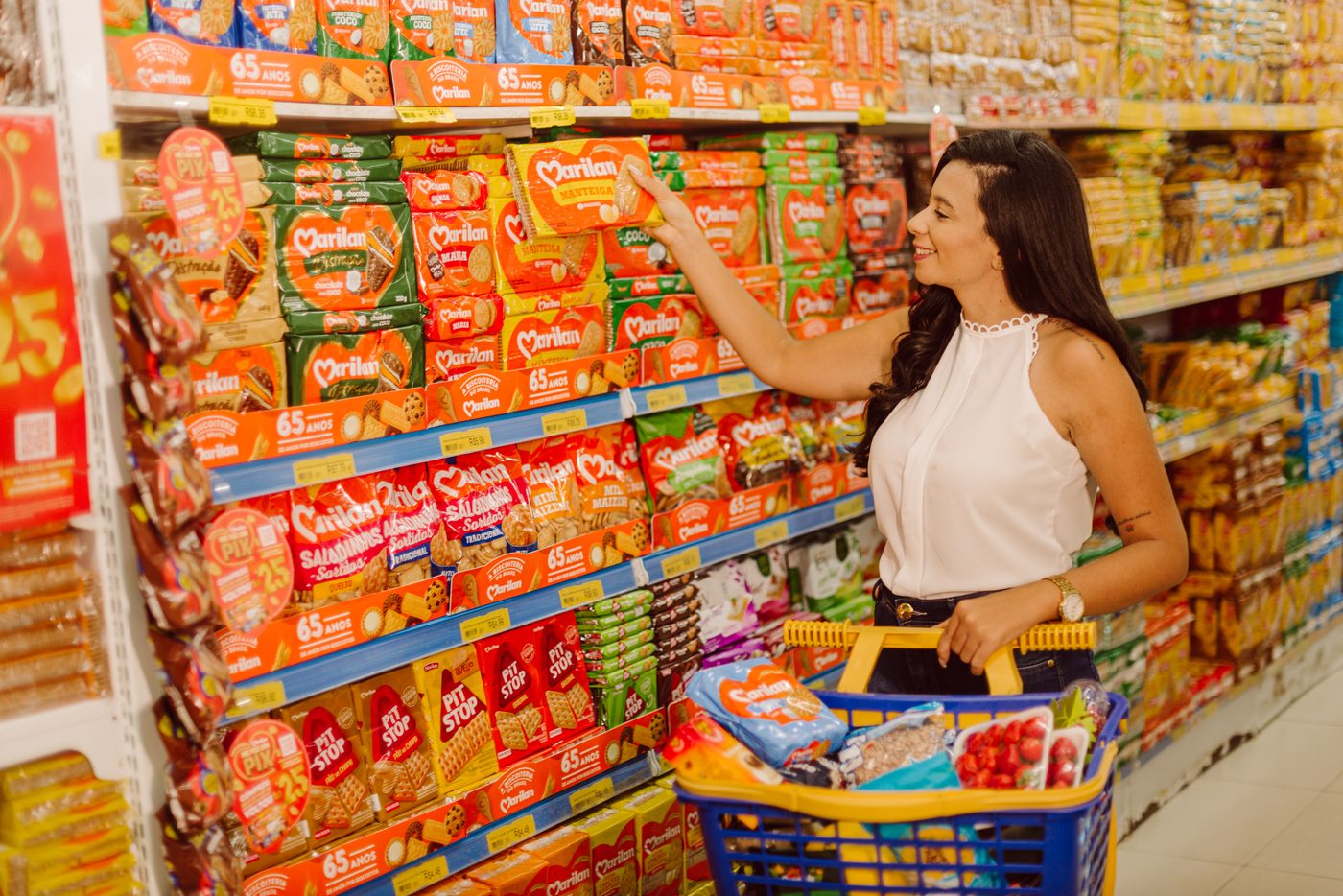 Cliente com o carrinho cheio entre as gôndolas abastecidas do Supermercado Aliança